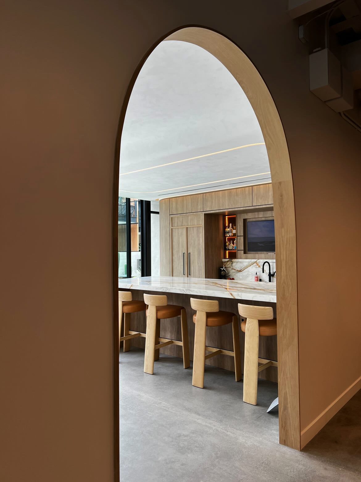 Arched doorway framing a kitchen with oak cabinetry, marble island and leather stools