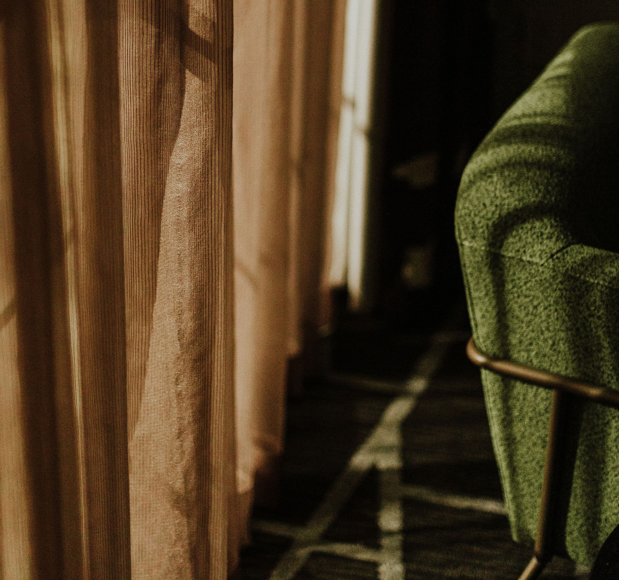 Sunlit interior with a green upholstered chair beside sheer curtains